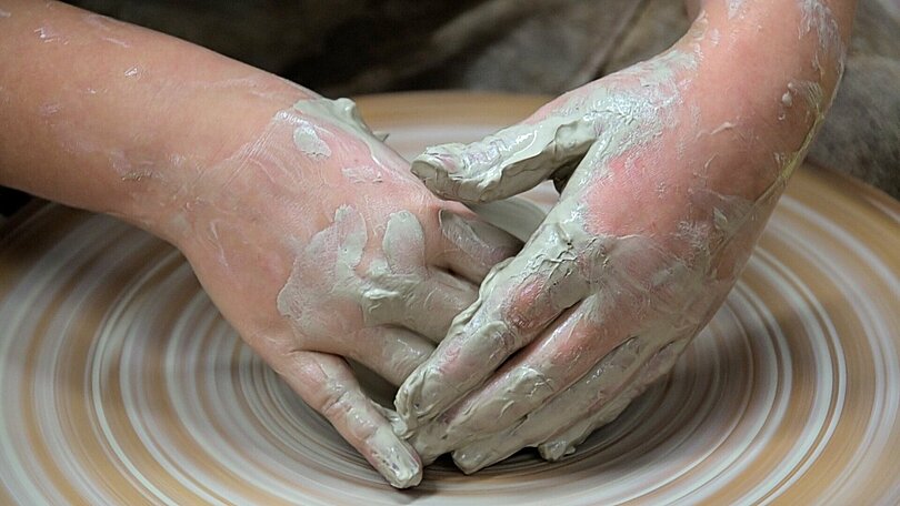 Zwei Hände arbeiten auf einer Töpferscheibe mit weißem Ton. 