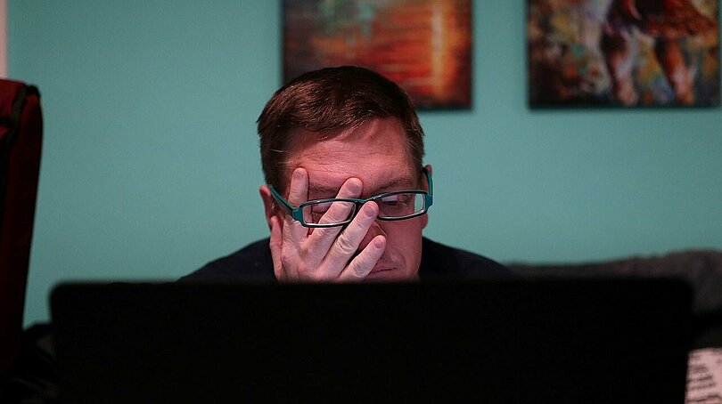 Ein Mann sitzt am PC und reibt sich müde die Augen.