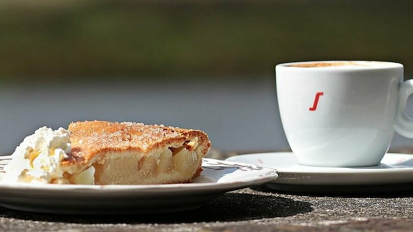 Ein Teller mit einem gedeckten Apfelkuchen und Schlagsahne und eine Tasse Kaffee 