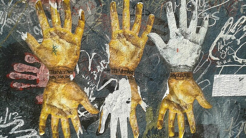 Kunstwerk durch Handabdrücke an der Berliner Mauer: Obere Reihe von links: zwei goldene und ein weißer Handabdruck schauen nach oben; untere Reihe von links: eine goldene, eine weiße und wieder eine goldene Hand schauen nach unten.