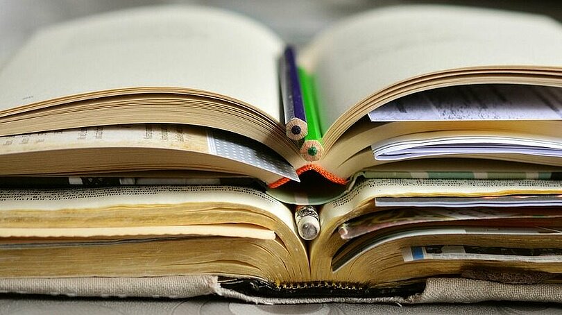 Ein Stapel aufgeschlagener Bücher mit eingelegten Stiften und Zetteln.