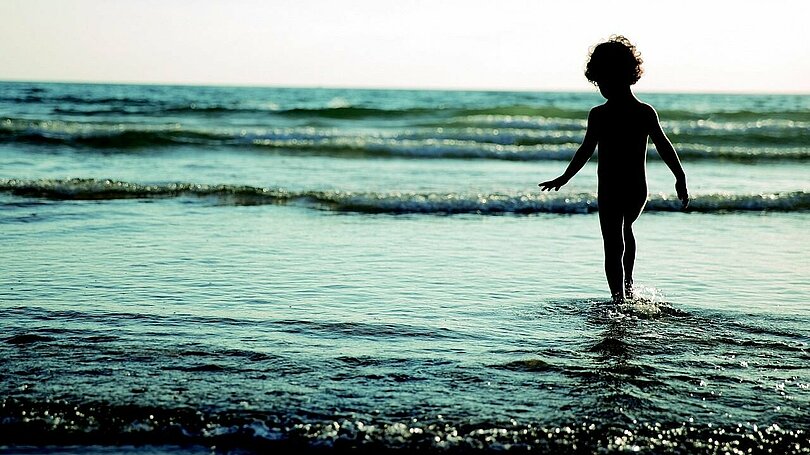 Ein Kind geht im seichten Wasser ein paar Schritte ins Meer hinein. 